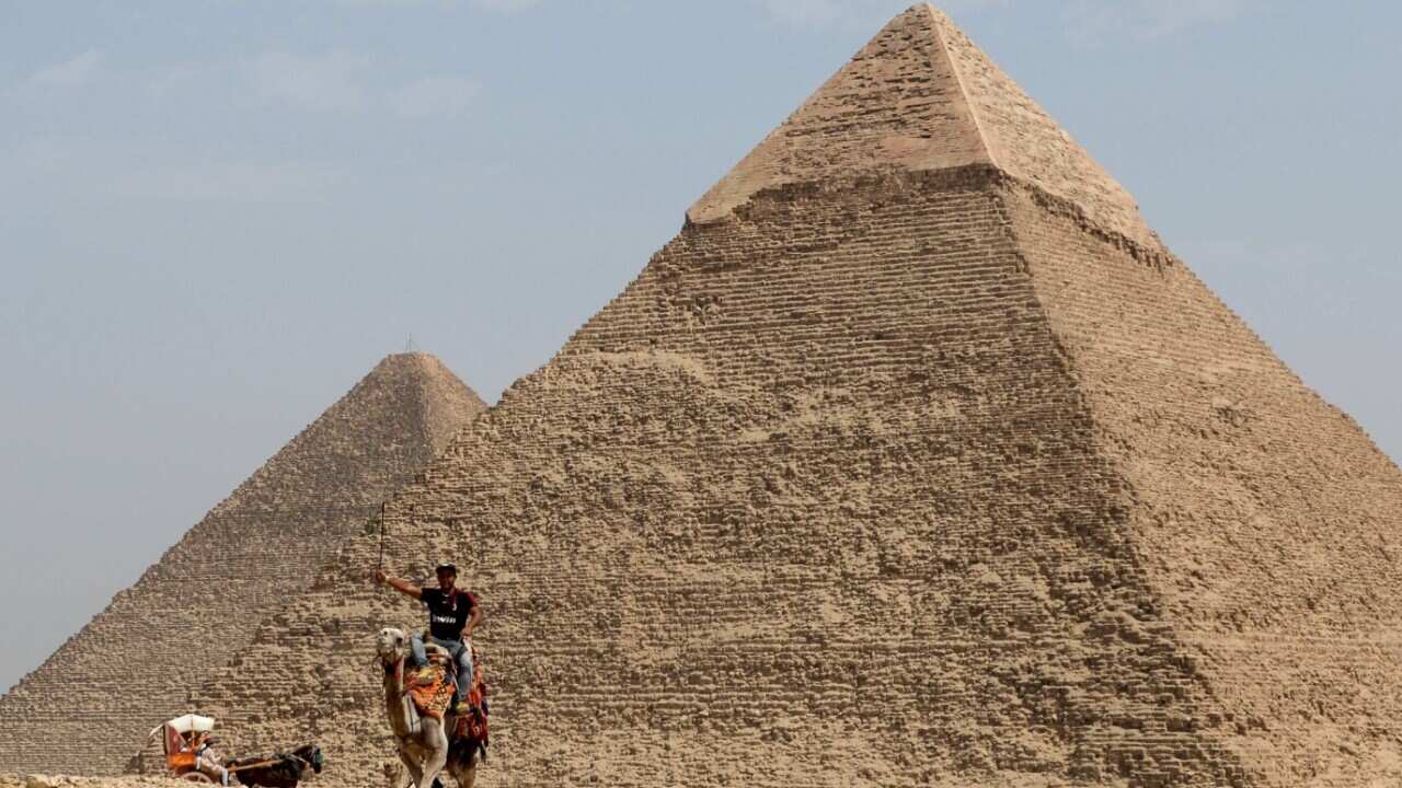 A man rides his camel in front of the pyramid of Khufu in Egypt