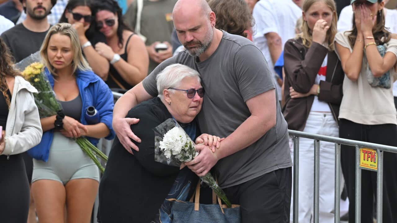 The grandmother of 10-year-old Matilda, who was killed in the Bondi terror attack, holds a bouquet of flowers and cries into the arms of a man at a memorial