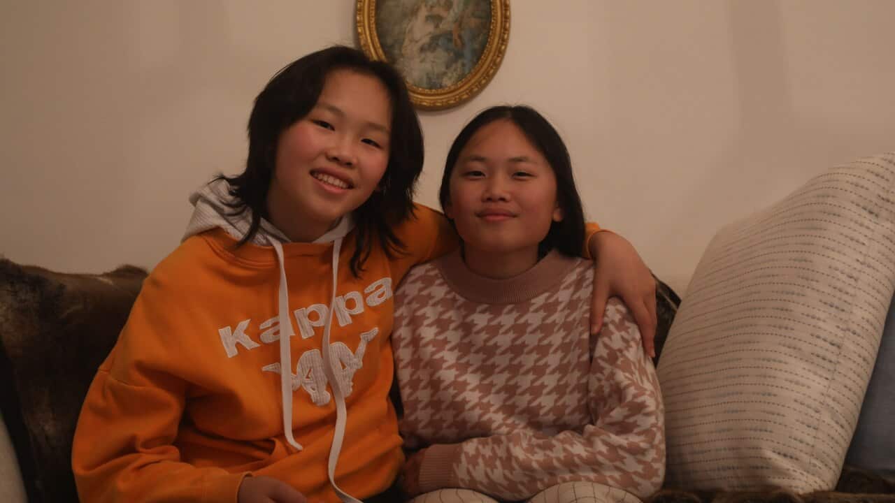 Jacqueline and her sister embrace on a couch smiling at the camera.