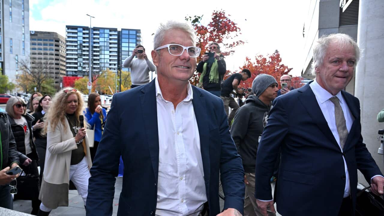 A man in a blue suit and white shirt, walking in front of a crowd