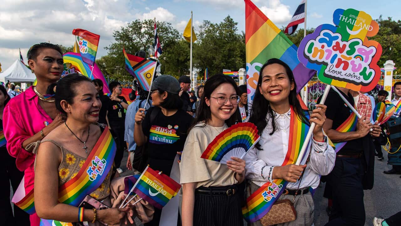 A group of people celebrating, many of them with rainbow-coloured flags.