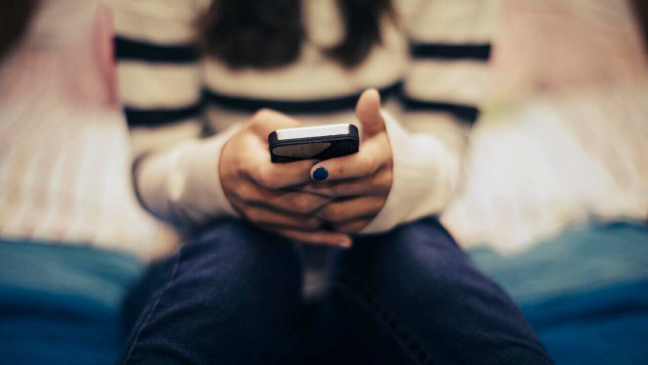 A close up of a teenager sitting on a bed using a smart phone