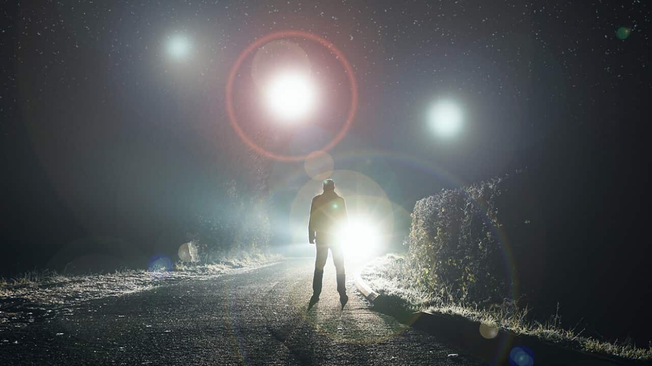 UFO concept. Glowing orbs, floating above a misty road at night. With a silhouetted figure looking at the lights.