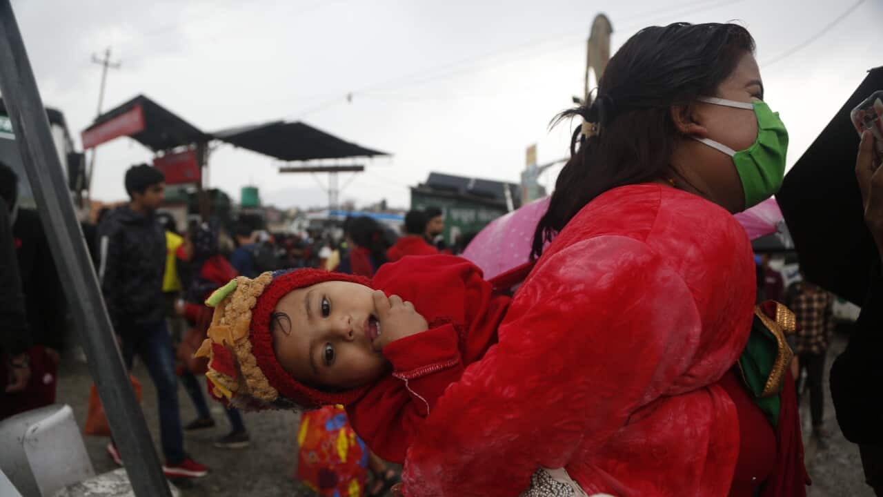 A Nepalese woman carries her child as she waits to board a vehicle during lockdown to prevent the spread of the new coronavirus in Bhaktapur, Nepal.