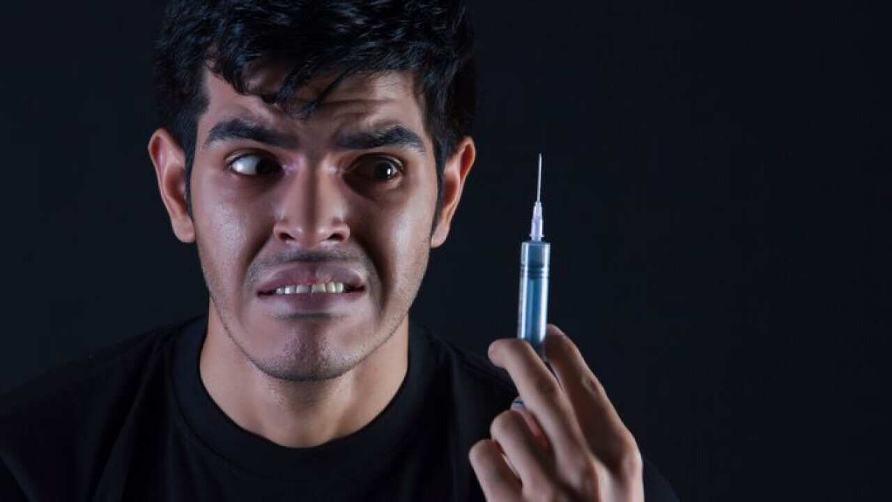 Fearful male drug addict looking at syringe against black background
