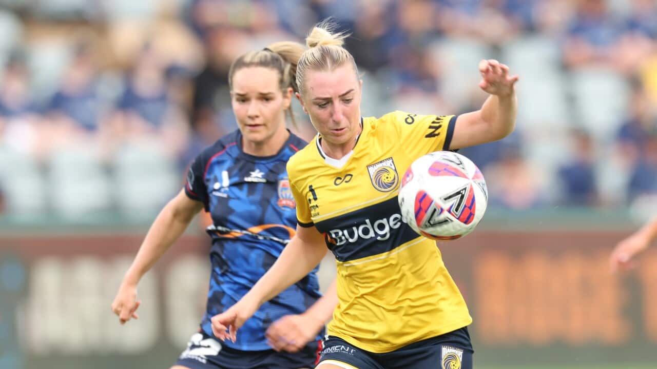 A woman in a yellow and blue football kit in front of another woman in a blue football kit during a match