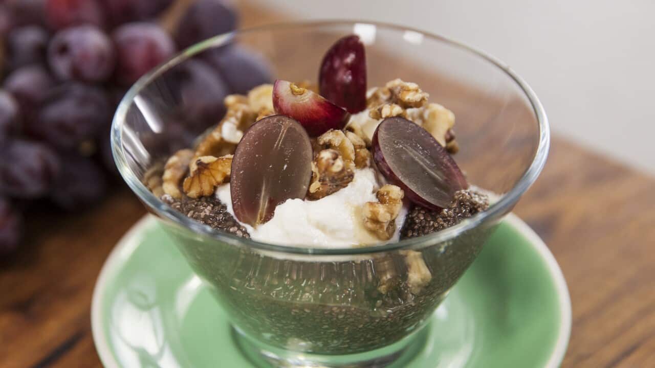 Chia pudding topped with yoghurt, walnuts and halved grapes sits in a glass bowl on a small green plate.