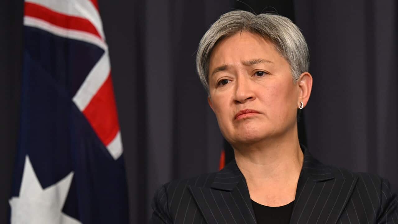 Penny Wong standing in front of a blue curtain and Australian flag.