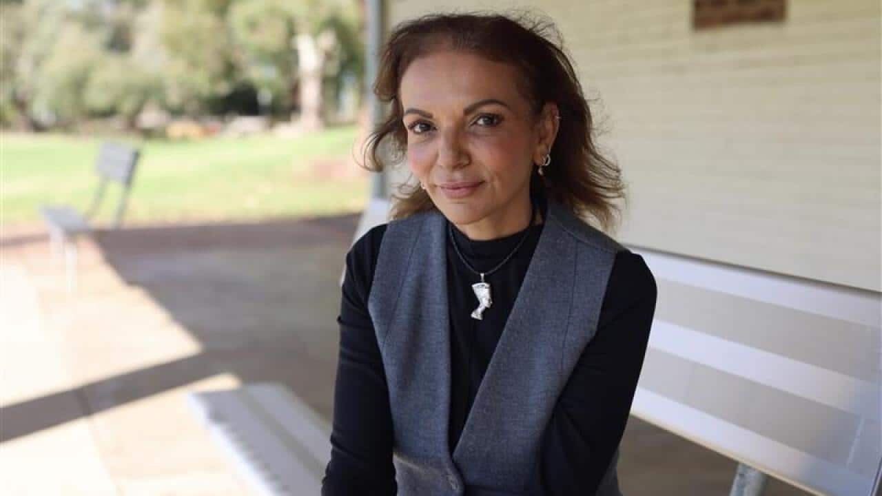 Headshot of Anne Aly wearing a white coat and black top and standing outside