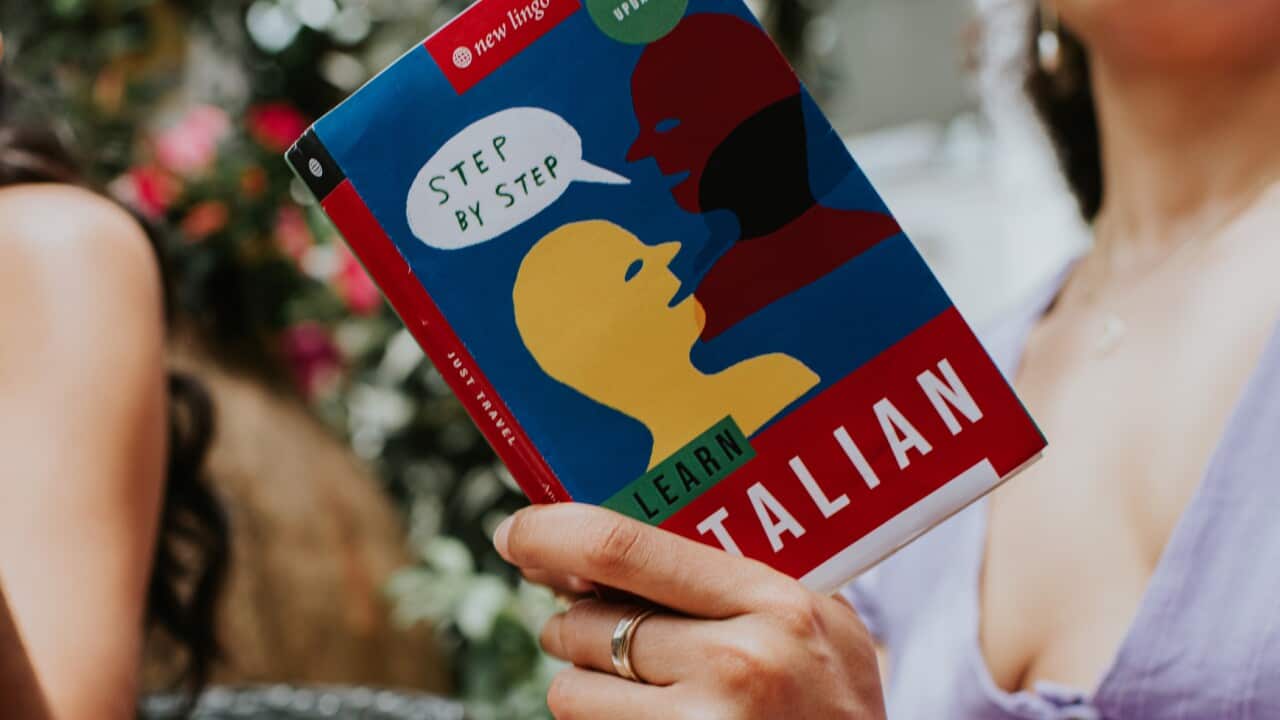 Two women read and discuss a Italian language book on a terrace