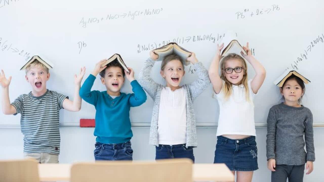 Happy pupils with books above their heads standing at whiteboard with formulas in class