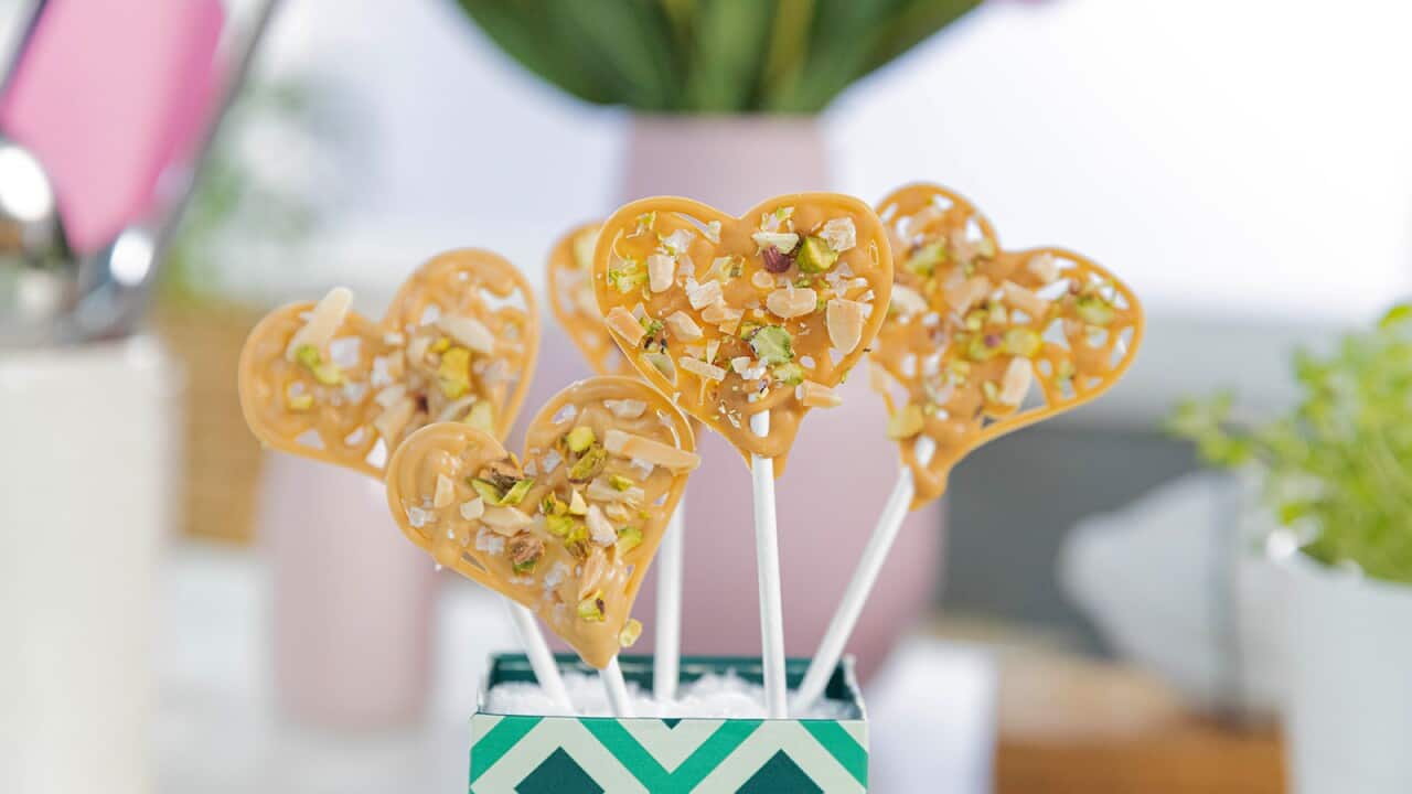 Five heart shapes made from swirls of caramel coloured chocolate top white sticks standing in a colourful box.