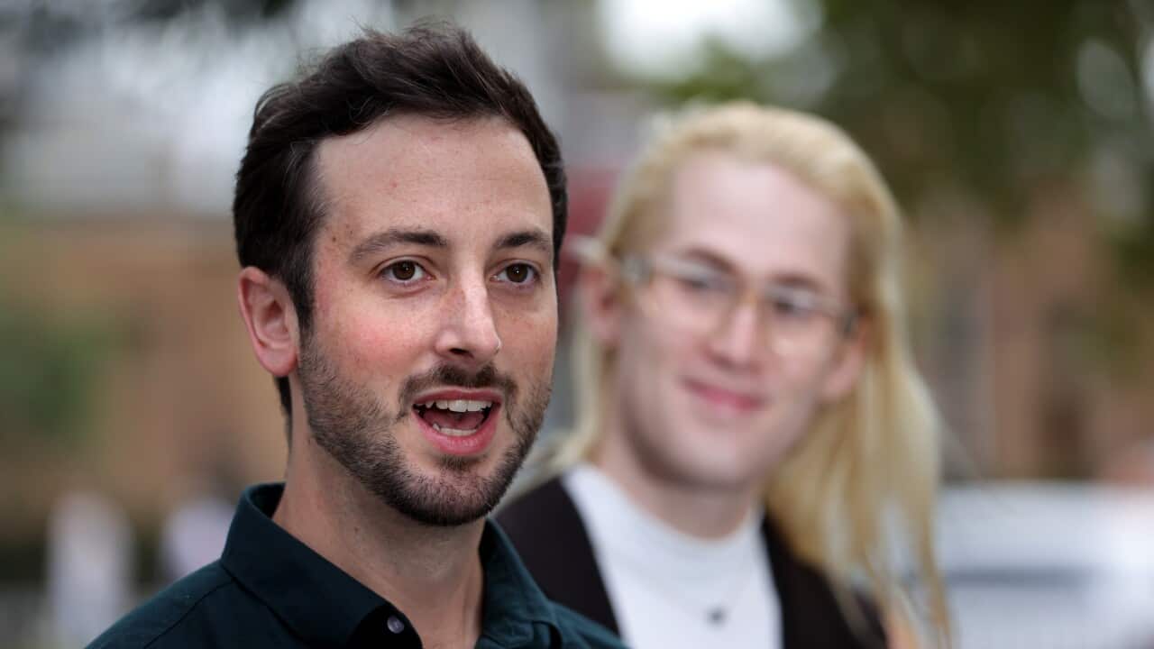 A man speaks as another person watches on.