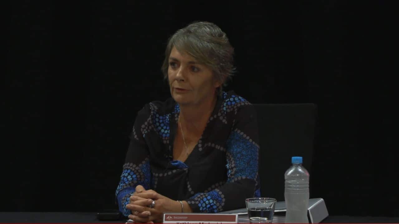A woman sits with her hands clasped