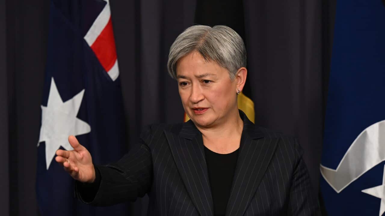 A woman in a dark pin stripped suits, looks and gestures towards her right.