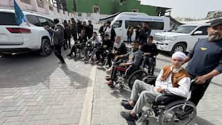 A group of men in wheelchairs waiting with trucks around them.
