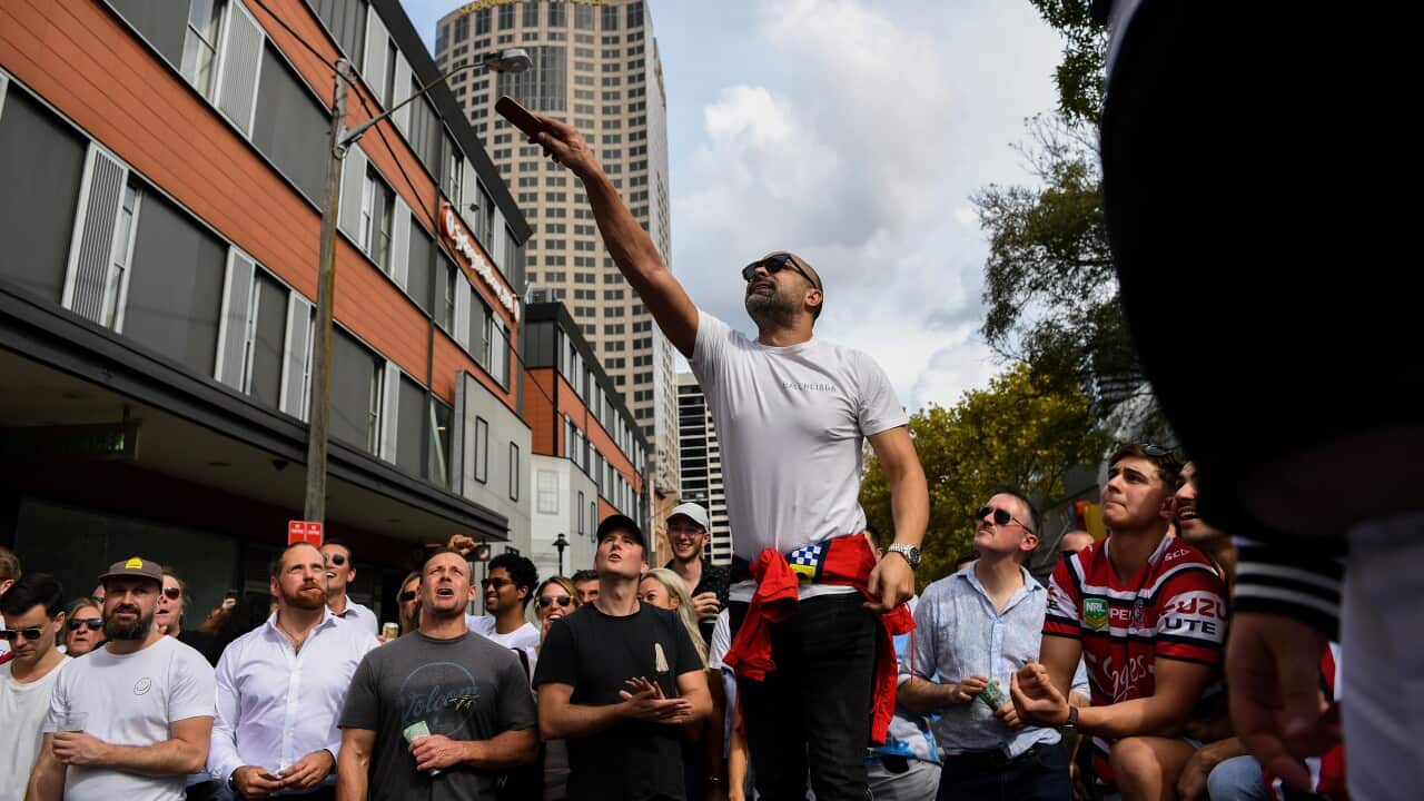 A man tosses two coins into the air while a crowd watches on.
