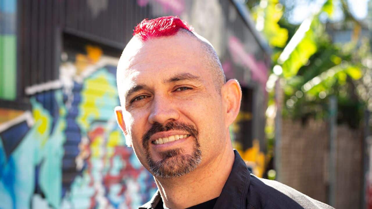 A man with a pink mohawk and black t-shirt smiles