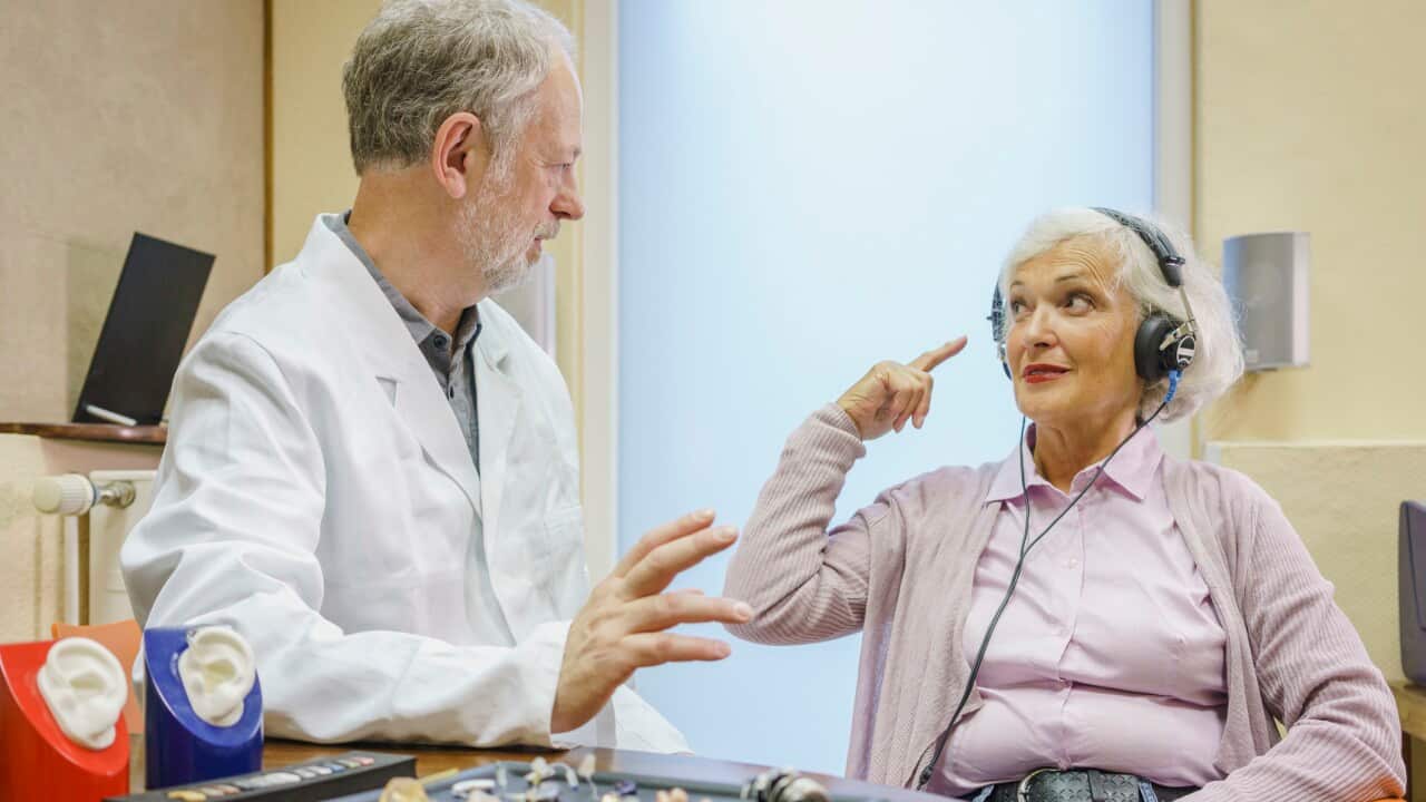 Senior patient wearing headphones talking to Audiologist during ear exam at doctors office