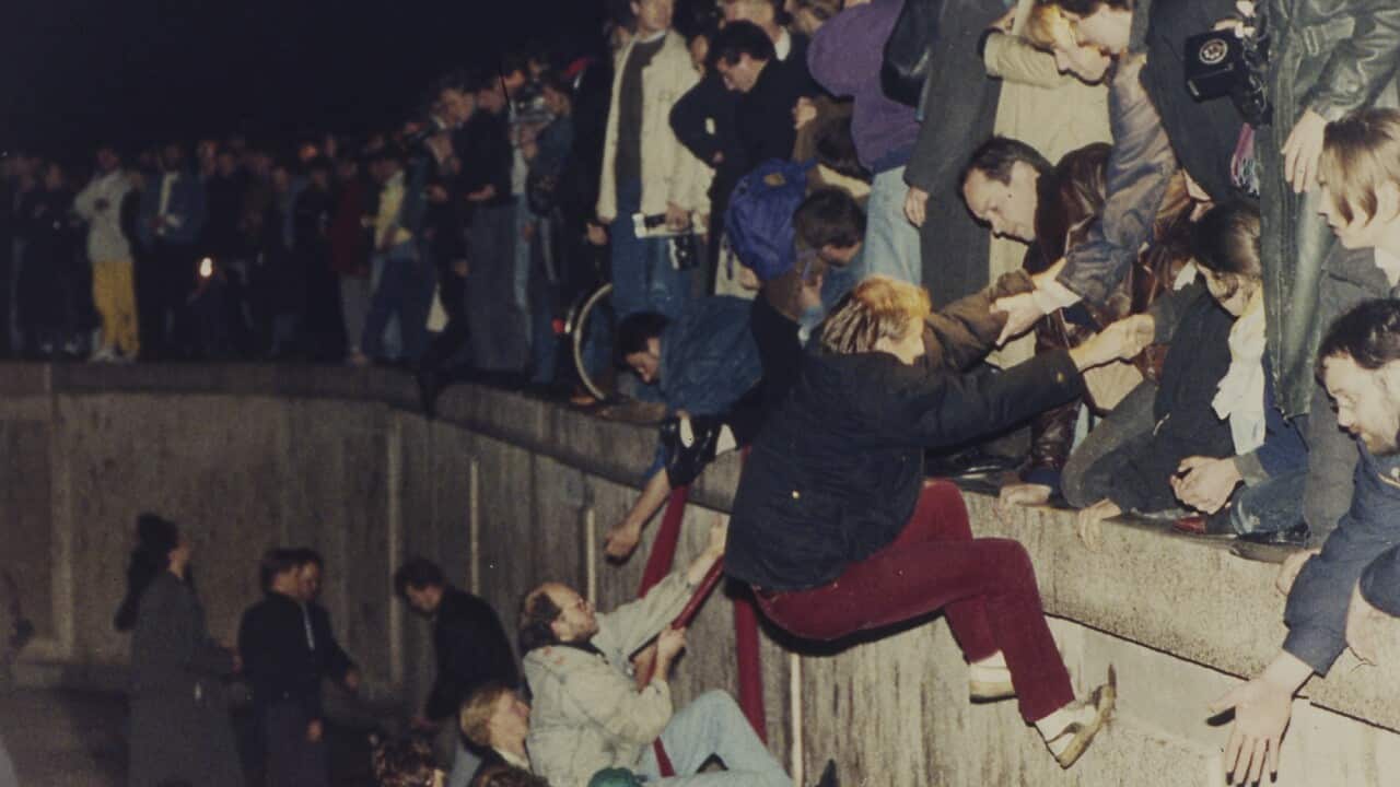 East Berliners get helping hands from West Berliners as they climb the Berlin Wall.