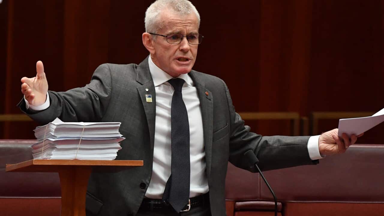 Politician gestures with his hands as he speaks in parliament holding some papers