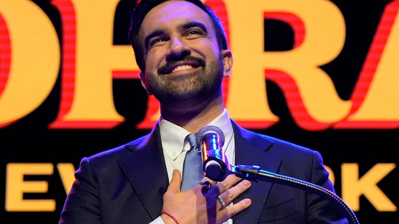 A man wearing a suit placed his hand on his chest while speaking to a microphone