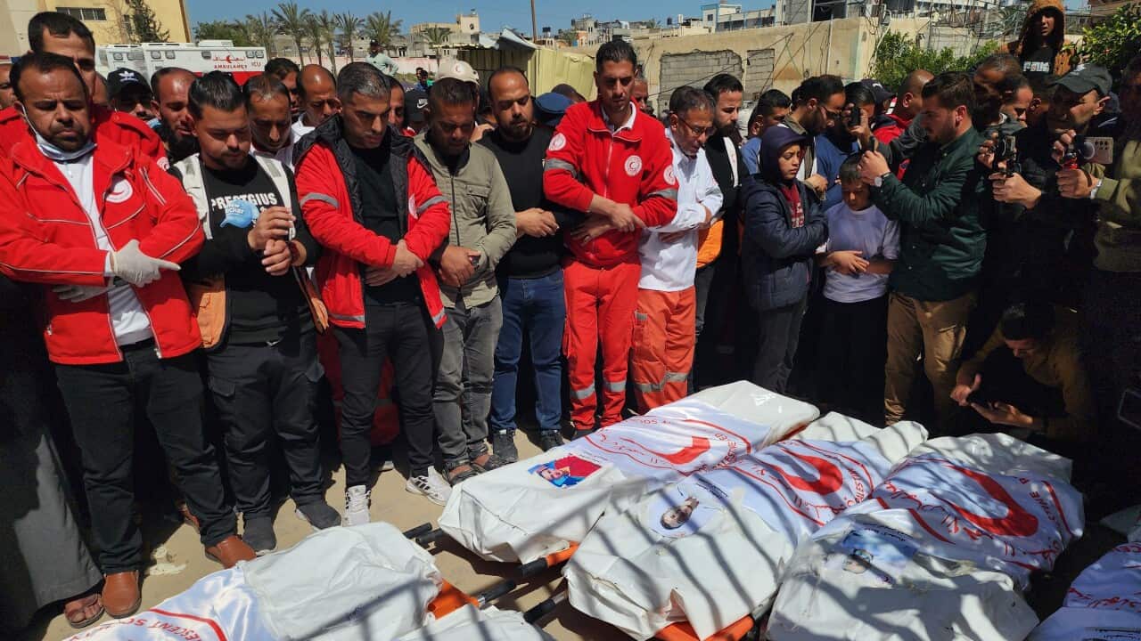 Workers in uniforms stand over body bags with red crescent symbol on them.