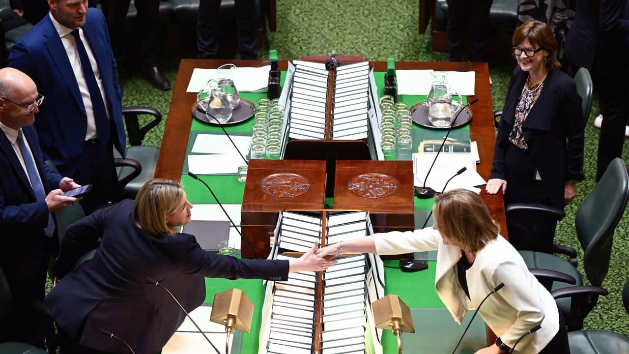 Aerial view of two women in a parliamentary chamber reaching across a table to shake hands