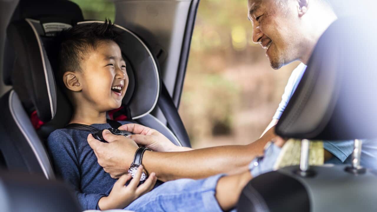Father buckling son in car seat