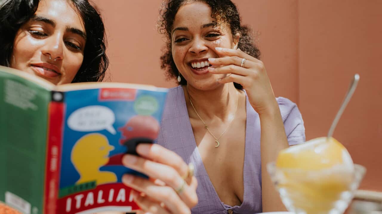 Two woman read and discuss a Italian language book on a terrace