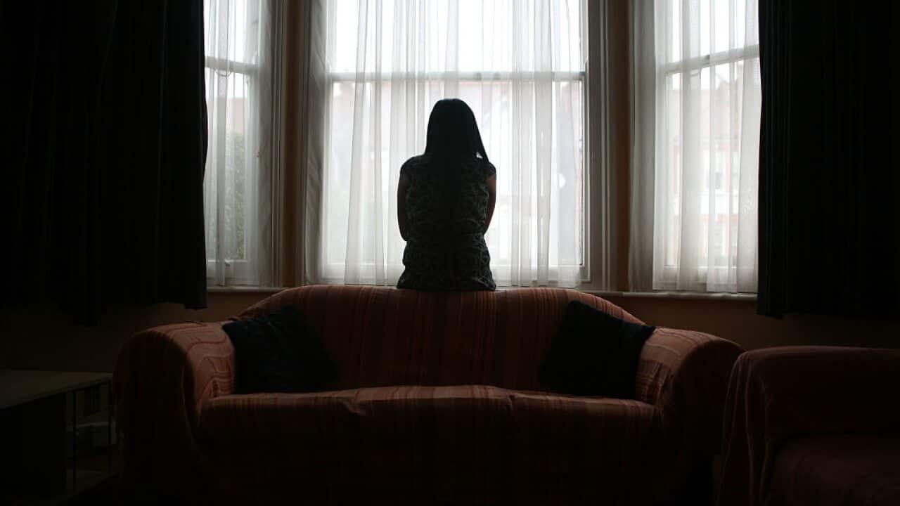 A young Asian woman suffering from domestic violence stands alone in the bay window of her home. (Photo by In Pictures Ltd./Corbis via Getty Images)