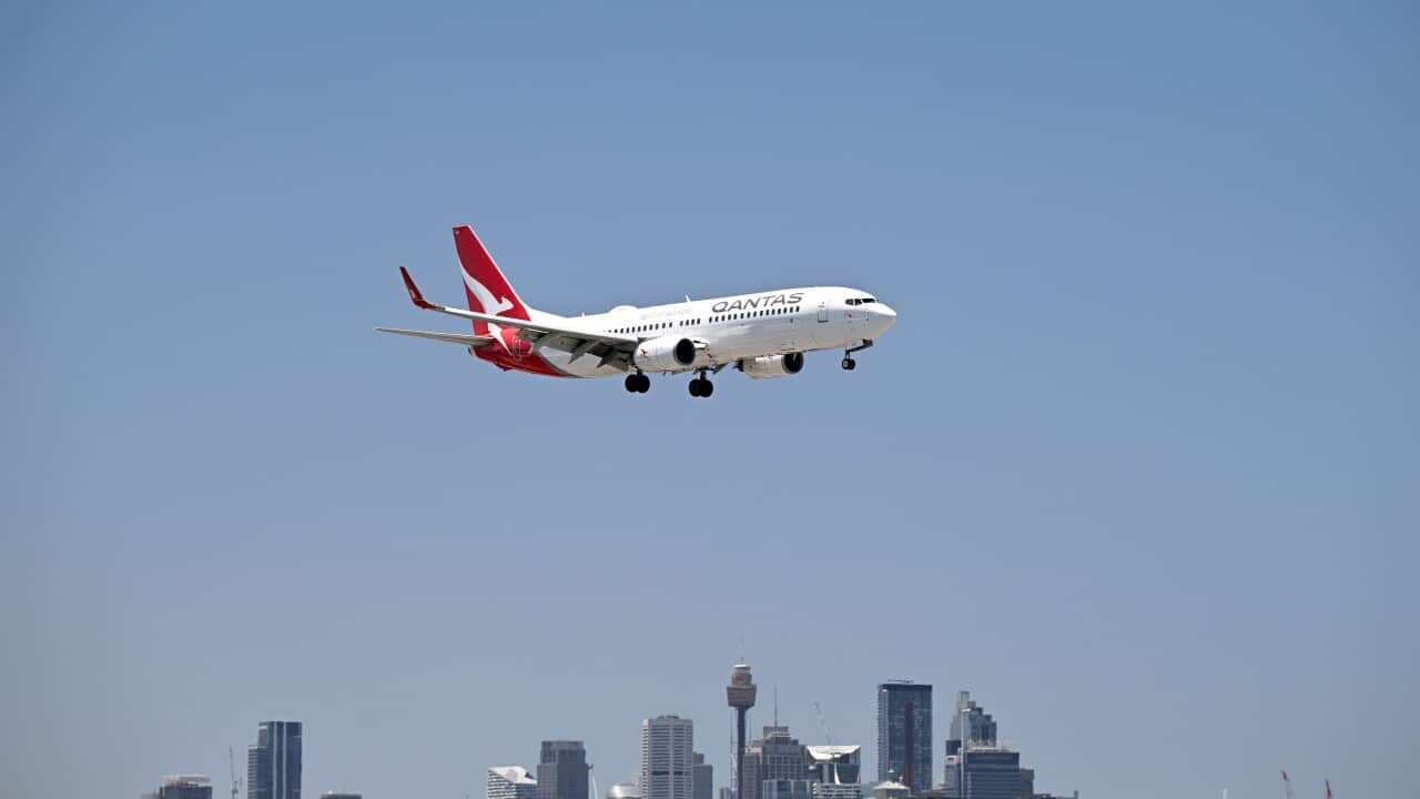An aeroplane flies over an airport with the city skyline seen in the background