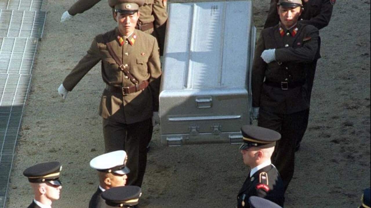 Military officers carry a metal casket