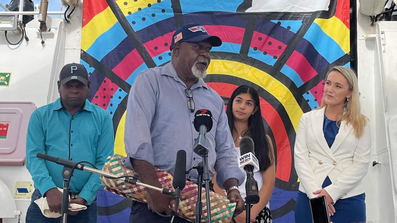 Two Torres Strait elders onboard a boat, standing next to a young South Asian woman and a blonde white woman.