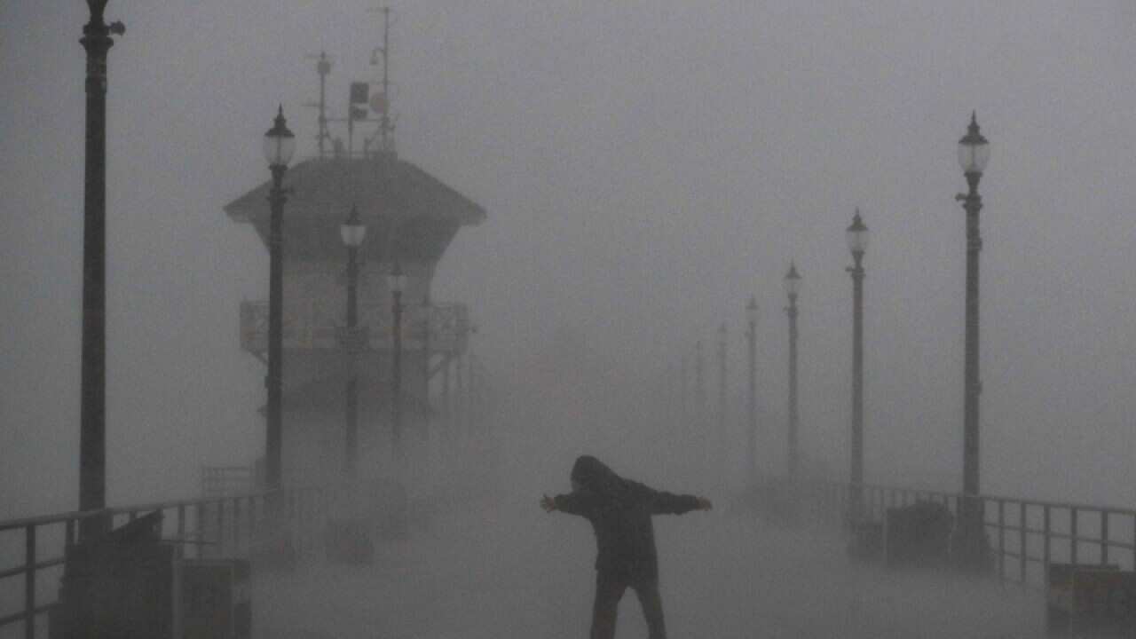 A man struggles against gusty wind and heavy rain in Huntington Beach