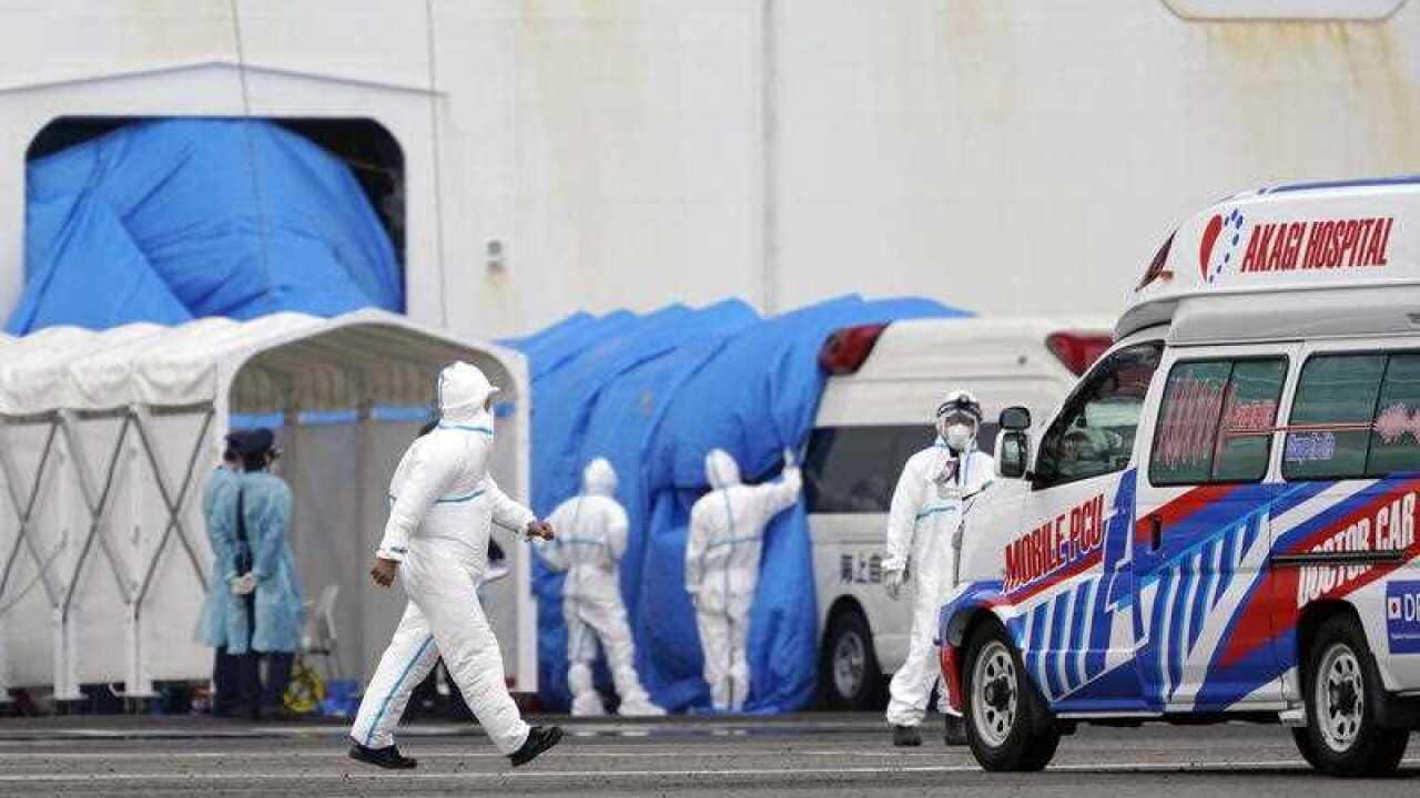 Personnel in protective gear walk towards the Diamond Princess cruise ship docked at the Daikoku Pier Cruise Terminal