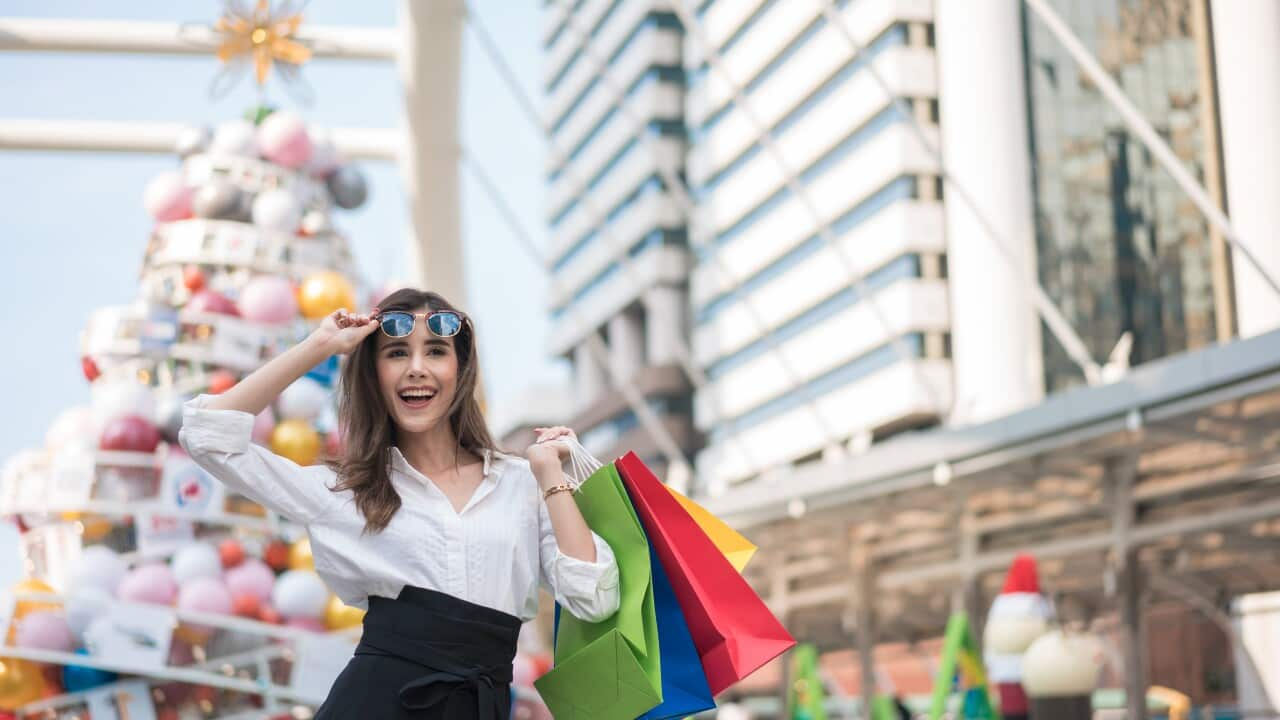 Portrait of an excited beautiful girl wearing dress and sunglasses holding shopping bags