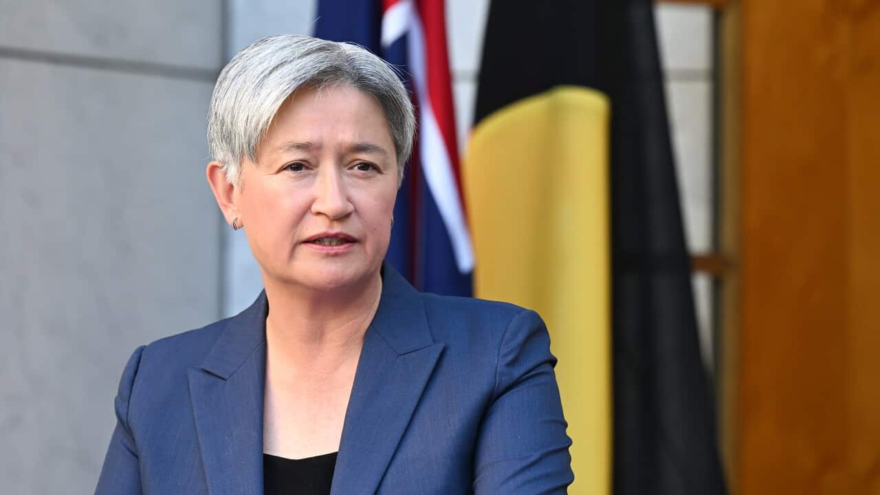 A middle-aged Asian woman with short grey hair. The Australian and Aboriginal flags are behind her.