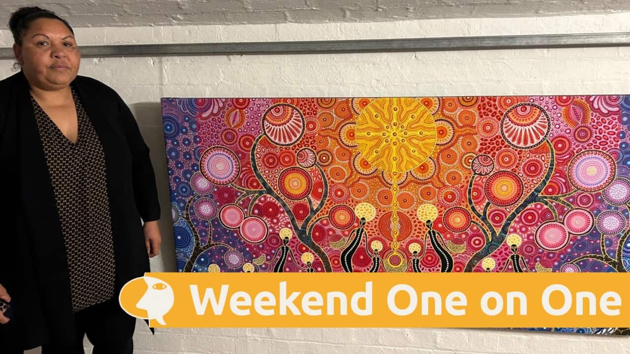 Artist Amunda Gorey standing next to a painting featuring rainbow colours and Dreamtime storytelling.