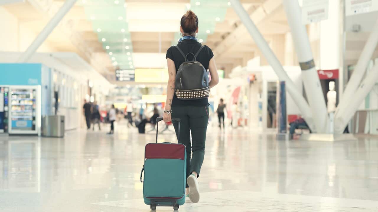 Back view of woman pulling her luggage strolling inside the airport terminal.