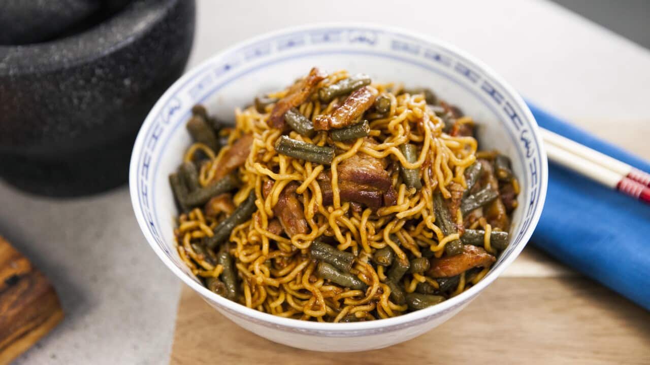 A delicious rich pile of noodles, beans and pork sits in a blue and white bowl.