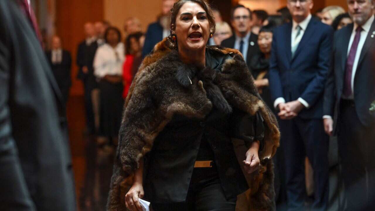 A woman draped in fur, yelling, with people around her.