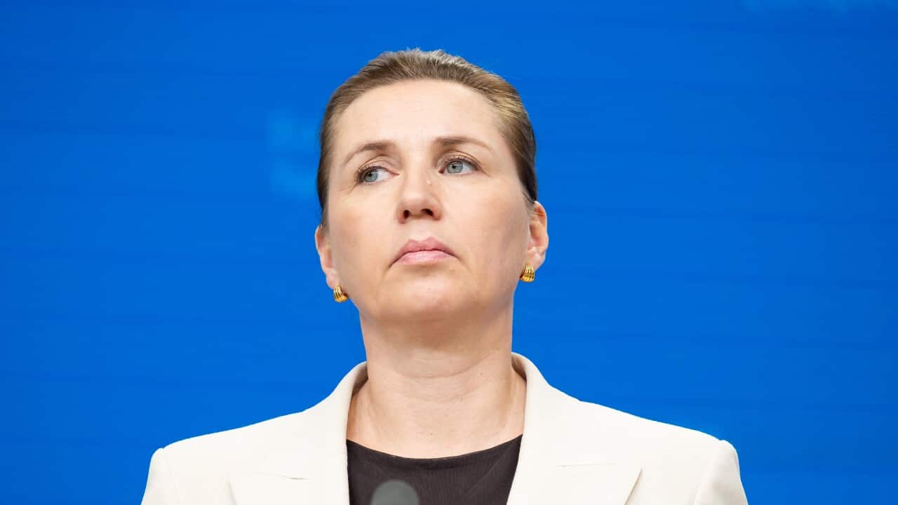 A woman looks on at a podium as she stands in front of a blue background.