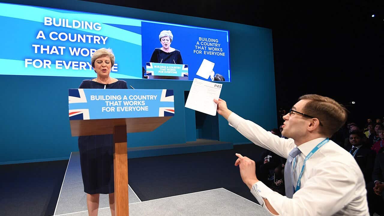A man holds a piece of paper with P45 written on it as Britain's Prime Minister Theresa May (L) delivers her speech.