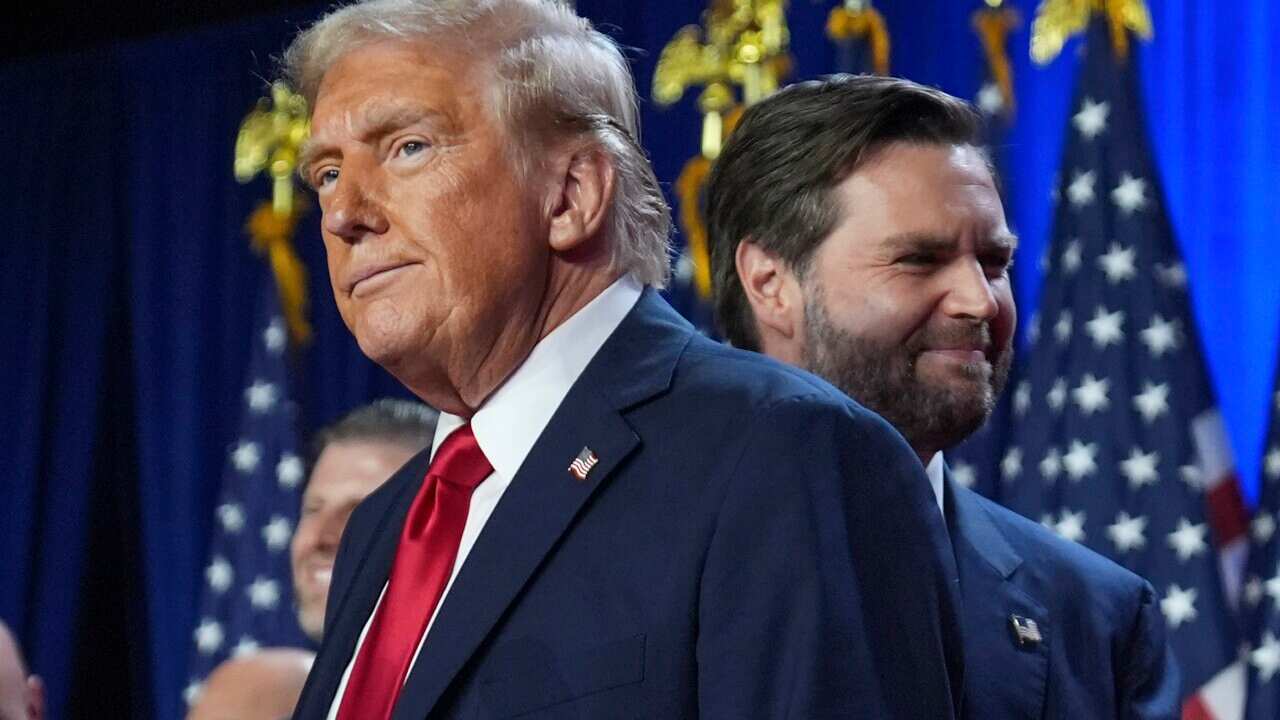 Two men wearing suits standing in front of American flags