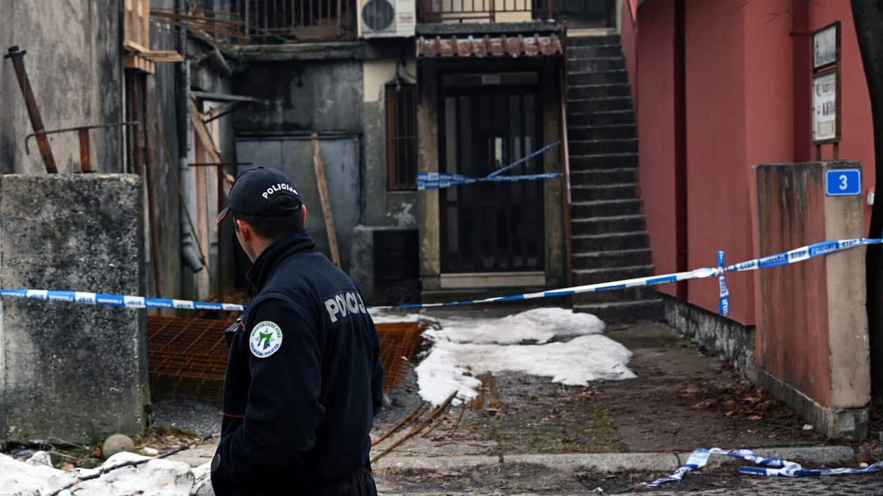 A police officer stands behind a row of police tape marking off a crime scene.