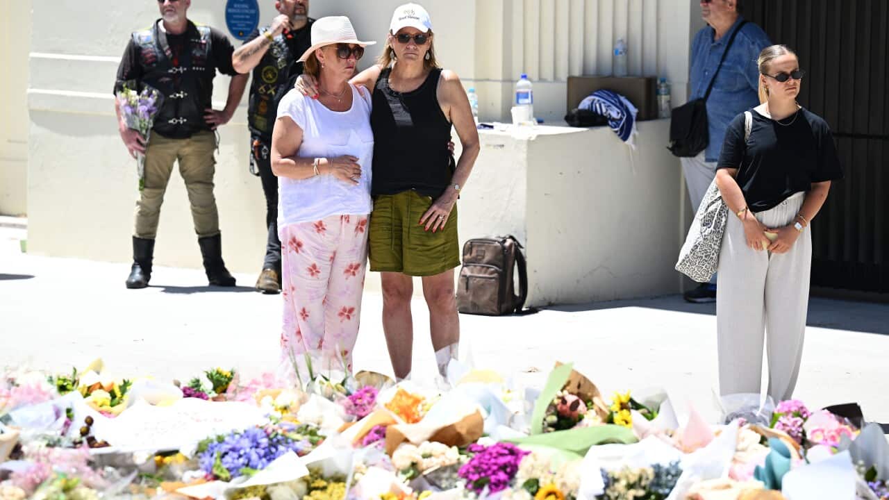 Women standing in front of a pile of flowers