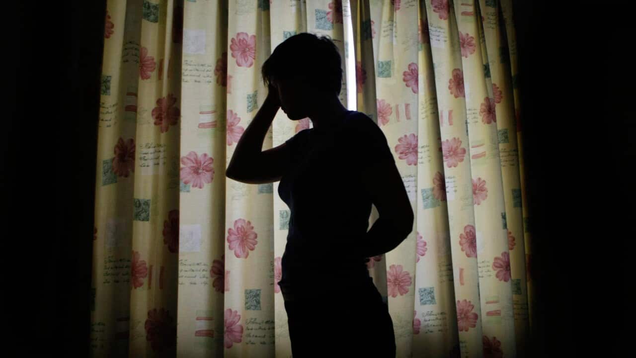 A silhoutte of a woman inside a room while holding her head