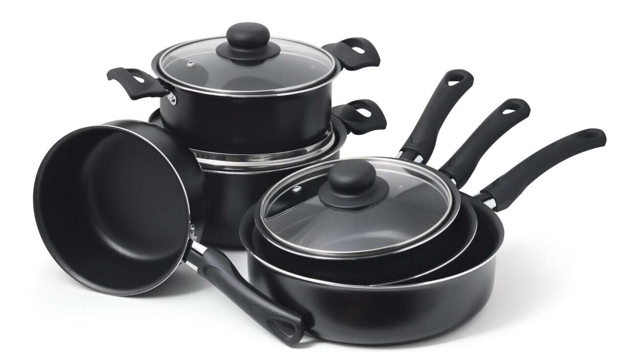 Set of black non-stick kitchen utensils on a white background. Pot, ladle, frying pan with glass lid.