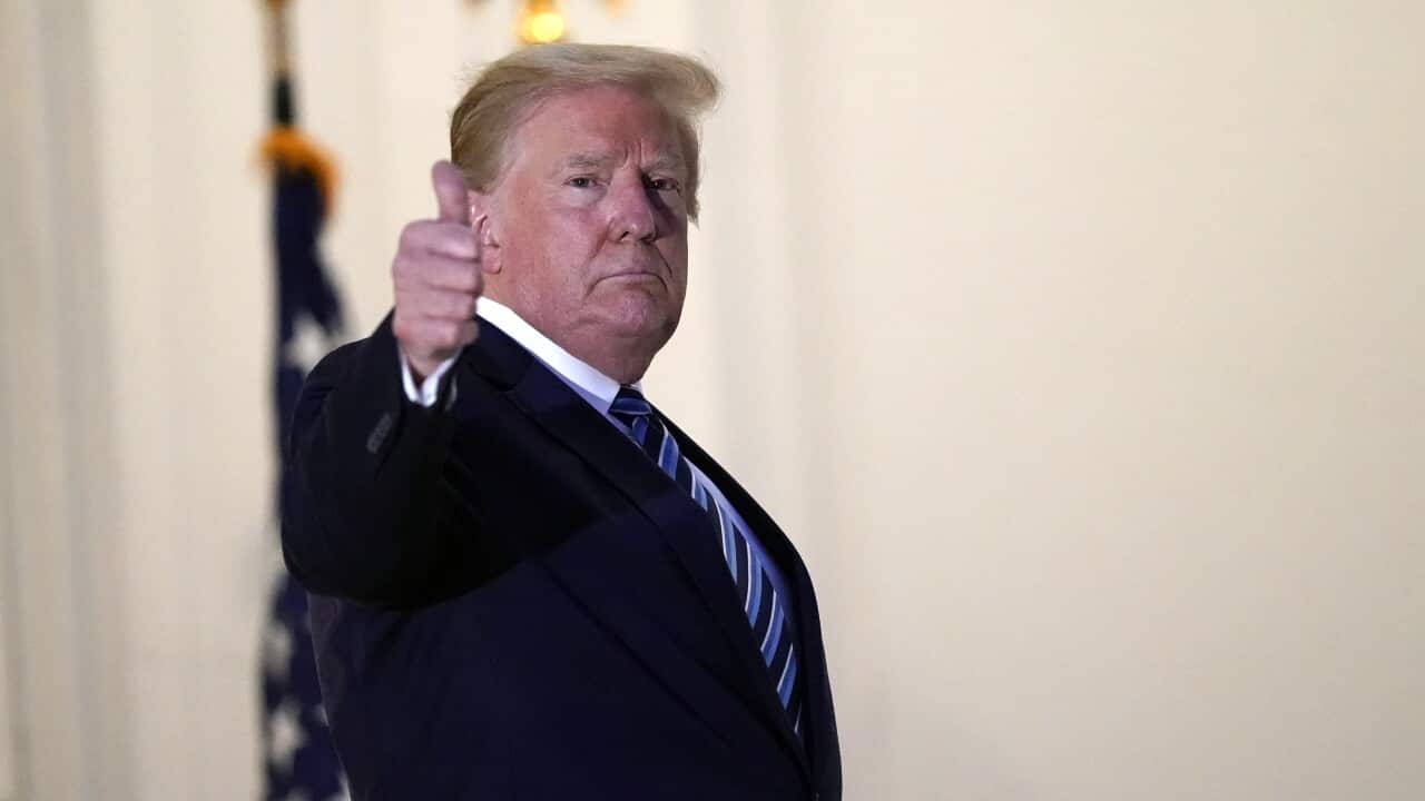 Donald Trump, wearing a dark suit, gives a 'thumbs-up' signal with his right hand